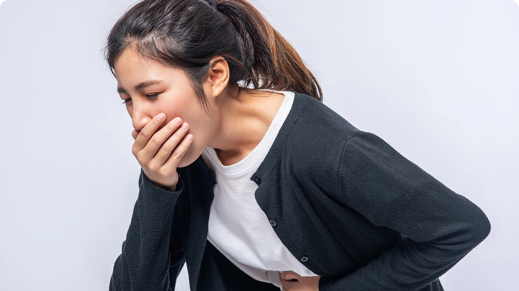 Man in a kitchen covering his mouth and vomiting into a sink.
