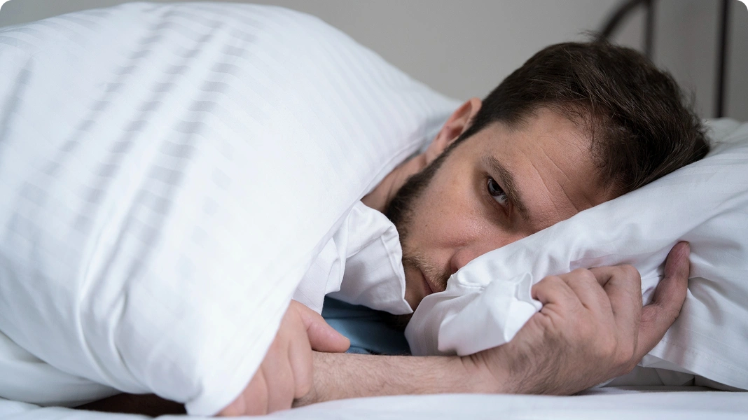 Man sitting on a bed in pajamas, holding his head in frustration or anxiety.
