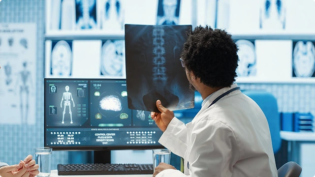 A patient lying on a medical scanner bed undergoing a bone density test, with a monitor displaying an image of the spine